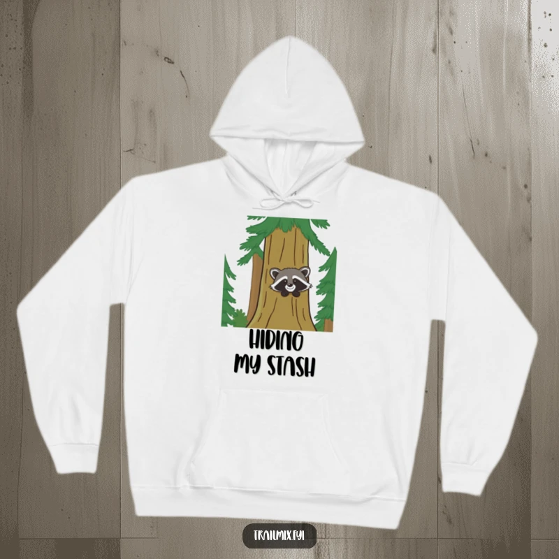 Funny hoodie shows a delighted raccoon peeking behind a large pine tree, offering cozy humor and woodland vibes.